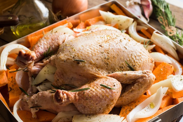 Uncooked whole chicken with chopped vegetables carrots sweet potatoes onions, seasoned