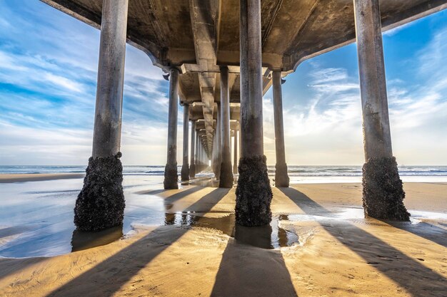 Photo the underside of the huntington beach pier in southern california shot during the sunset casts long shadows across the golden sand