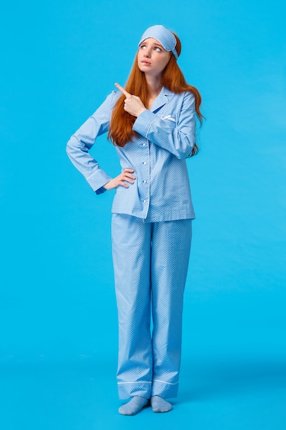 Uneasy and worried, concerned upset redhead female in nightwear and sleep mask