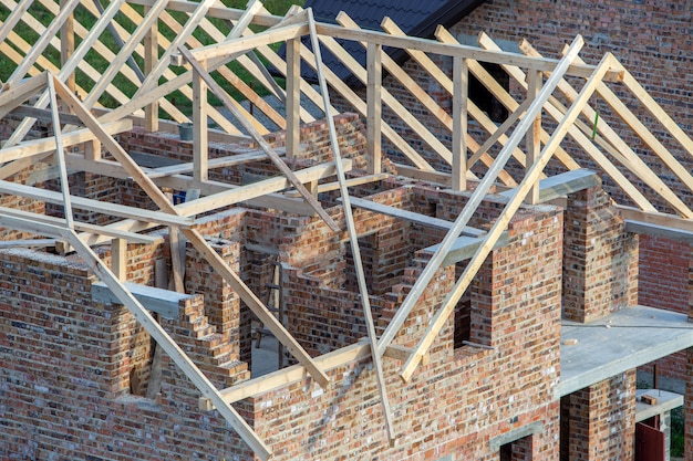 Unfinished brick house with wooden roof structure under construction.