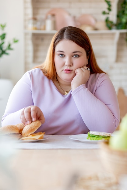 Unhappy chubby woman holding her cheek while taking a hamburger