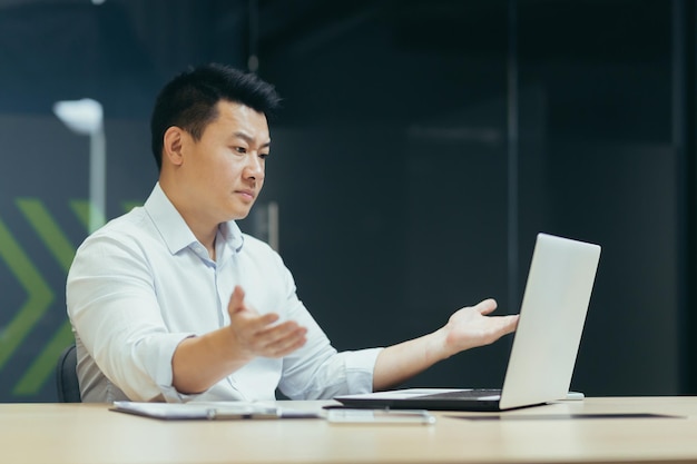 Unhappy and disappointed asian businessman looking at laptop screen and waving hands nervously man