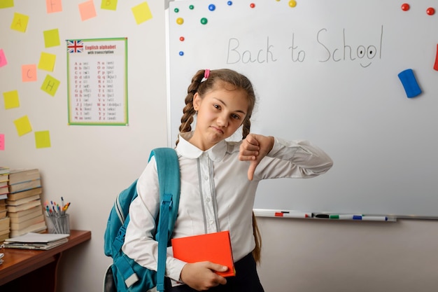 Unhappy female secondary school learner with books and a backpack showing thumbs down