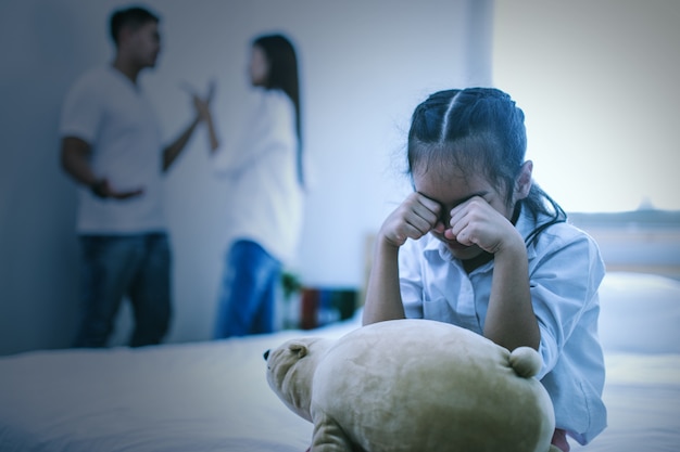 The unhappy girl sitting near the arguing parents on the bed