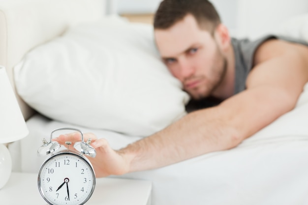 Unhappy man switching off his alarm clock