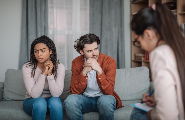 Unhappy millennial caucasian husband ignores black wife at psychologist consultation