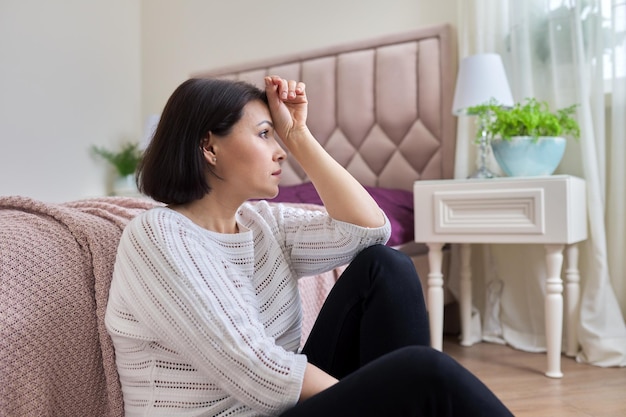 Unhappy tired depressed mature woman sitting at home on the floor