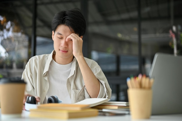 Unhappy and upset young Asian male college student sits at the coffee shop preparing for an exam