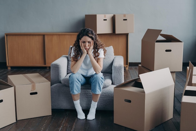 Unhappy woman is sad because of relocation sitting near cardboard boxes Hard moving day divorce