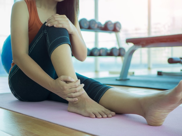 Unhappy woman sitting on the yoga mat with ankle  injury.