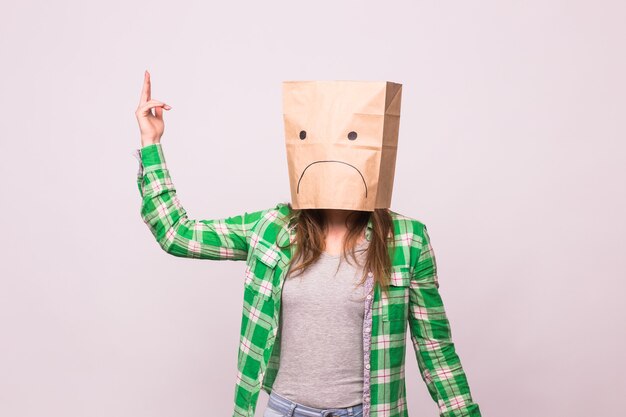 Unhappy woman with sad emoticon in front of paper bag on her head on white background