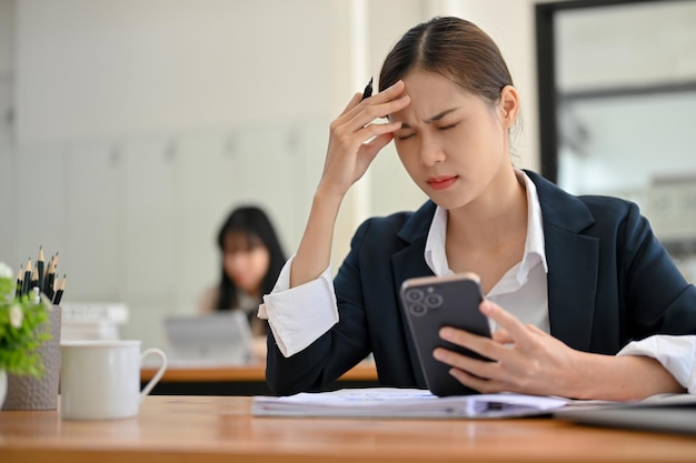 Unhappy young Asian businesswoman at her office desk suffering from a headache