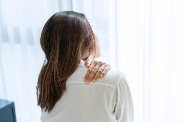 Unhappy young Asian woman suffering from shoulder pain on bed after wake up in the morning