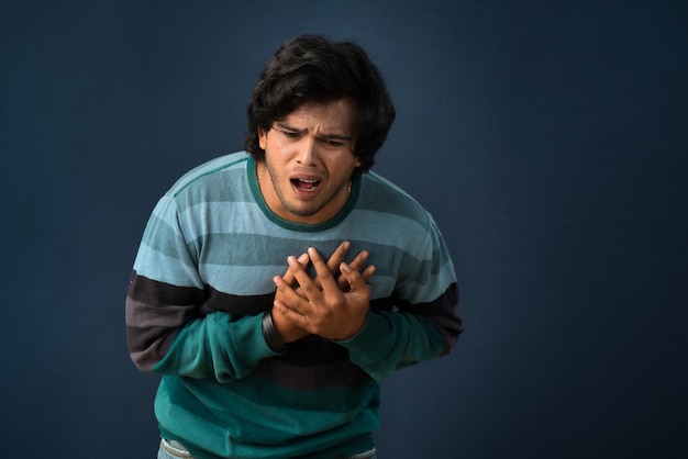 Unhappy young man having a heart attack or heartache over gray background People healthcare and health problem concept