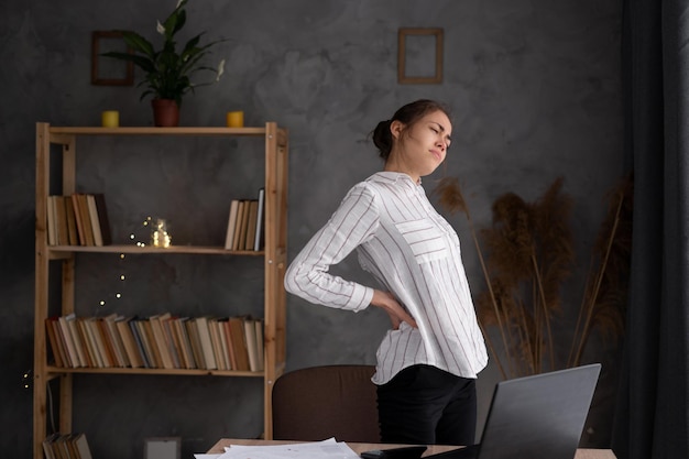 Photo unhappy young woman suffering from backache problem after long hours sedentary work frustrated upset woman employee worker standing in modern office back pain