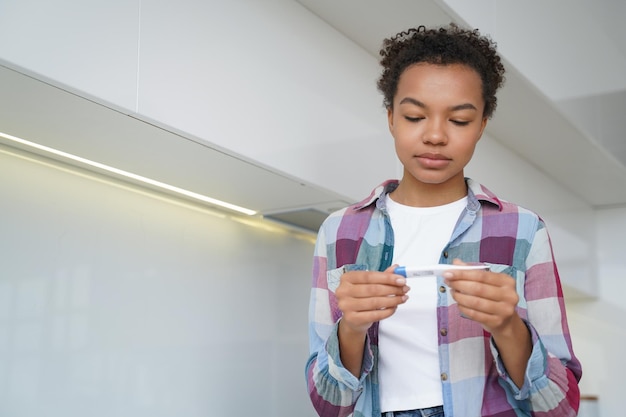 Unhealthy mixed race teen girl check body temperature with digital thermometer standing at home