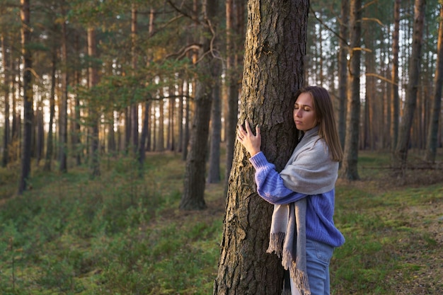 Unity with nature young calm girl hugging pine tree trunk with closed eyes walking in autumn forest