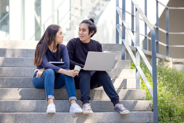 In the university campus, two Asian couples sit on the stairwell with their thumbs up, working on laptops.