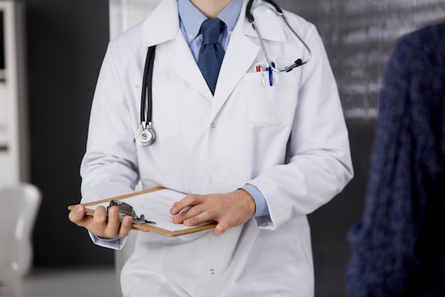 Unknown bearded doctor and patient woman discussing current health examination while sitting in sunny clinic, close-up. Medicine concept.