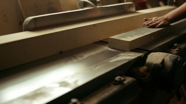 Unknown carpenter cutting wood in carpentry workshop Closeup unrecognized man preparing plank in studio Handyman working on wood lathe machine indoors in slow motion