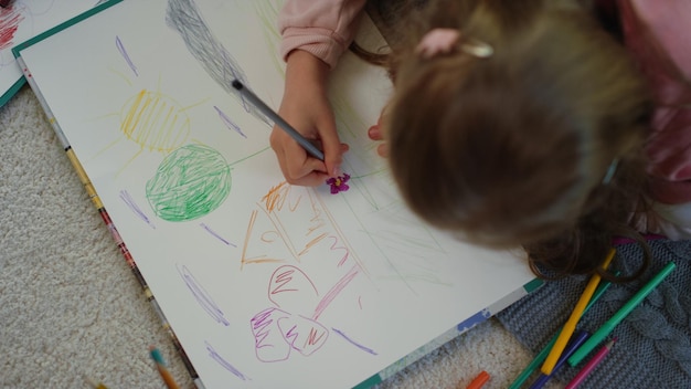 Unknown girl lying floor with colored pencils Creative kid drawing picture home