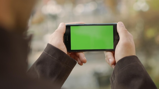 Unknown guy holding smartphone with chroma key screen outside Closeup man hands touching mobile phone with green screen outdoor Unrecognizable male person having video call by mock up cellphone