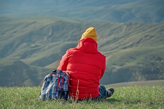 An unknown man sits in a clearing against the backdrop of mountains