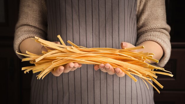 Unknown woman in apron with yellow raw spaghetti fettuccine