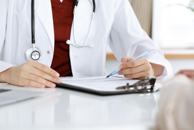 Unknown woman-doctor consulting patient and using clipboard with a medication history record. Medicine concept