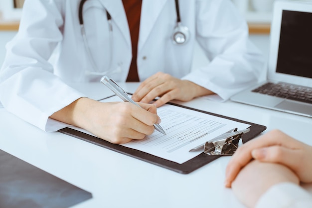 Unknown woman-doctor filling up an application form while consulting patient. Medicine concept.