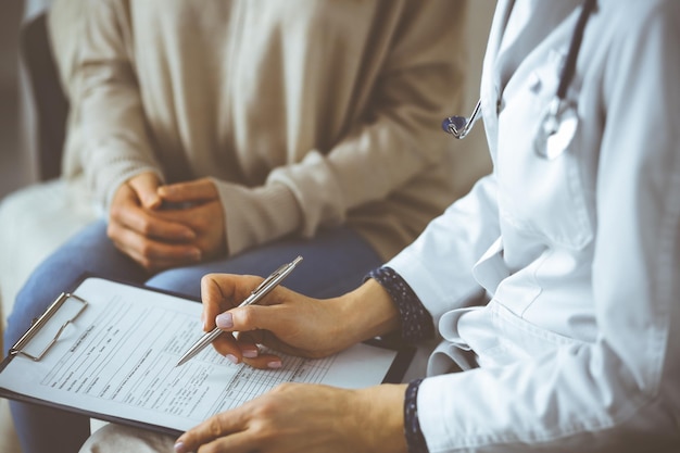 Unknown woman-doctor and patient discussing current health examination while sitting indoors. Stay at home concept during Coronavirus pandemic and self isolation quarantine.