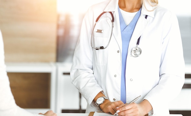 Unknown womandoctor and patient in sunny hospital Physician controls medication history records and exam results while using clipboard closeup