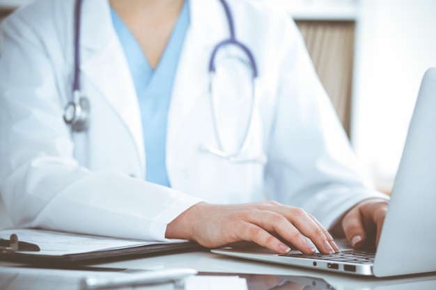 Unknown womandoctor typing on laptop computer while sitting at the table Medicine concept