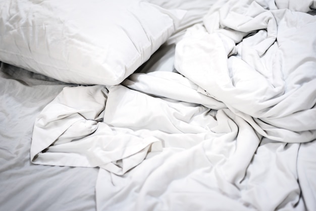 Unmade bed in the morning with sunrise  , white pillow on bed and with wrinkle background messy blanket in bedroom