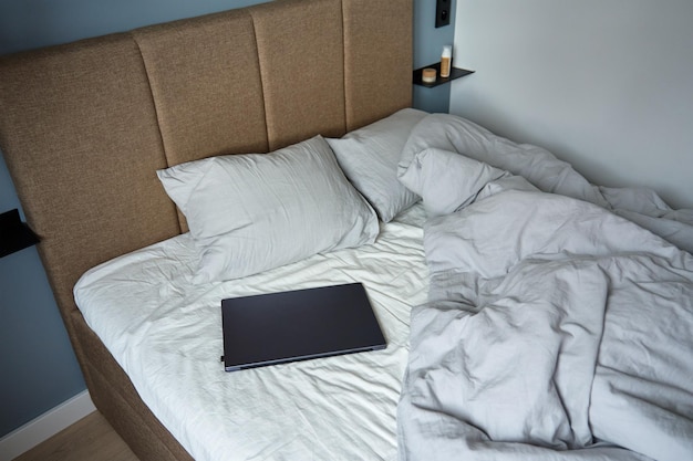 Unmade bed with pillows and crumpled bedsheets and open laptop