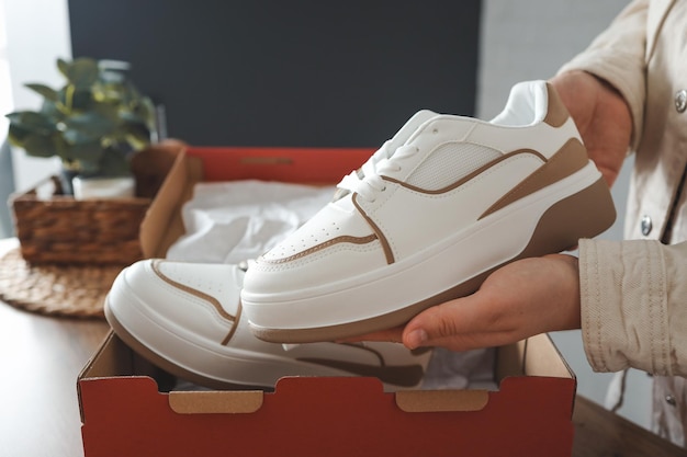 Unpacking women's shoes stylish white sneakers in hands