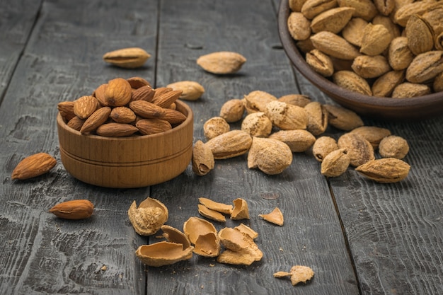 Unpeeled almonds spilling out of the bowl and a cup of peeled almonds