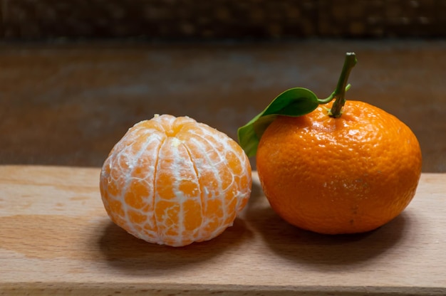 Unpeeled and peeled tangerines on a wooden tray