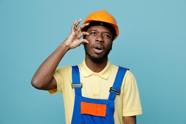 Unpleased putting hand on face young african american builder in uniform isolated on blue background