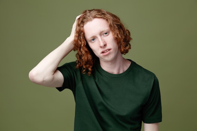 Unpleased putting hand on head young handsome guy wearing green t shirt isolated on green background