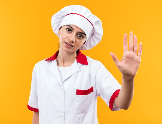 Unpleased young beautiful girl in chef uniform showing stop gesture 