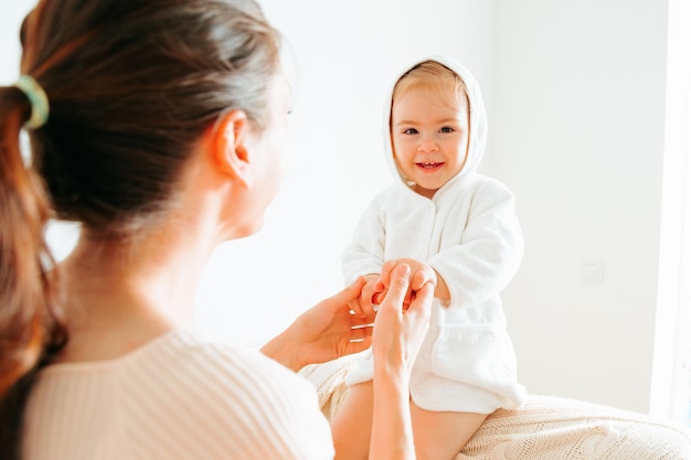 Unrecognizable adult woman support hands of little girl sit on edge baby smile happy look at camera