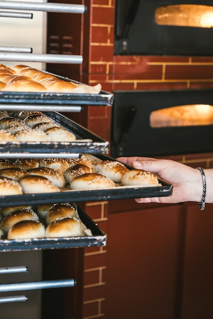 Unrecognizable baker puts bread on shelf Fresh buns from the oven Baking bread Transportation of baking