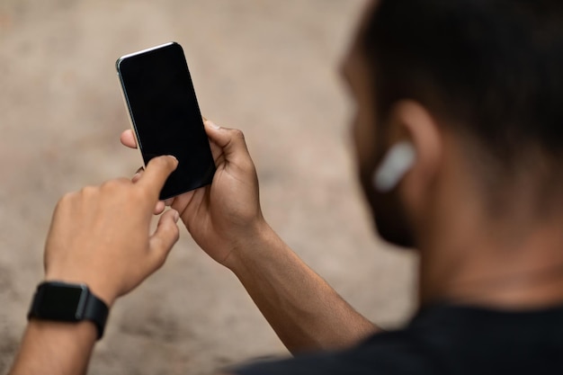 Unrecognizable black sportsman using cell phone with blank screen