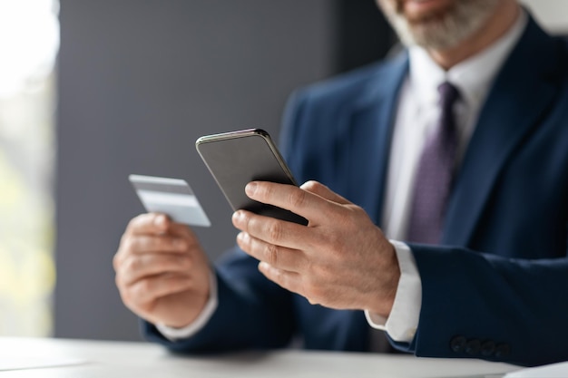 Unrecognizable Businessman Making Online Payments With Credit Card And Smartphone In Office