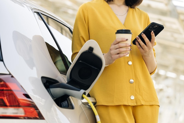 Unrecognizable caucasian woman using smart phone and waiting power supply connect to electric car