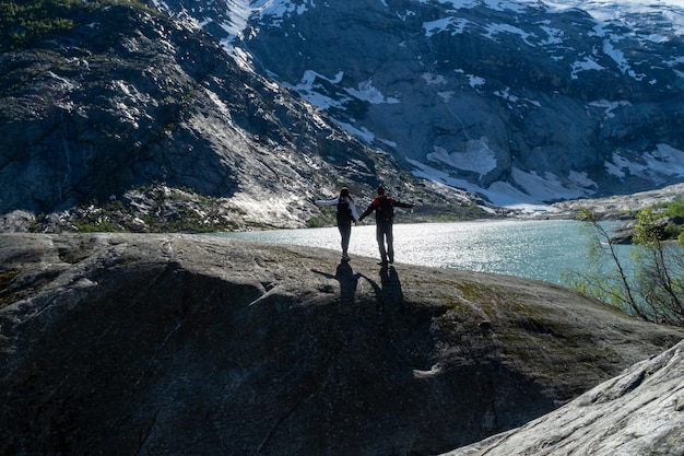 Unrecognizable couple of backpackers on top of a rock with the glacier river in the background with their arms raised