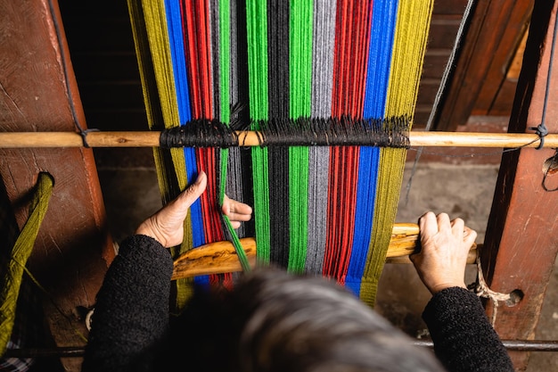 Unrecognizable elder woman's hands using a homemade craft loom to weave colorful wool