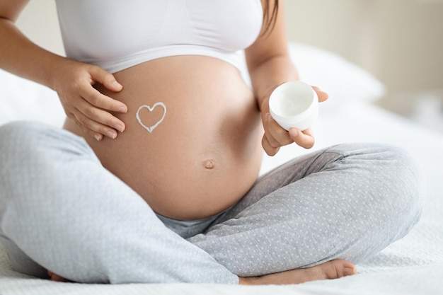 Unrecognizable expecting lady applying belly butter on her big tummy