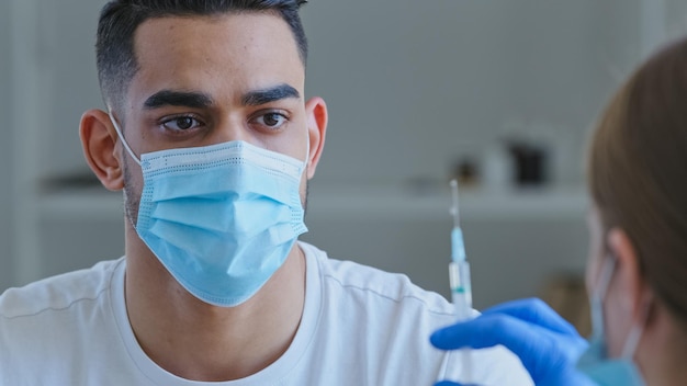 Unrecognizable female doctor in gloves holds syringe with vaccine medicine getting ready make vaccination injection from covid19 coronavirus to sick arab hispanic man patient in medical mask close up